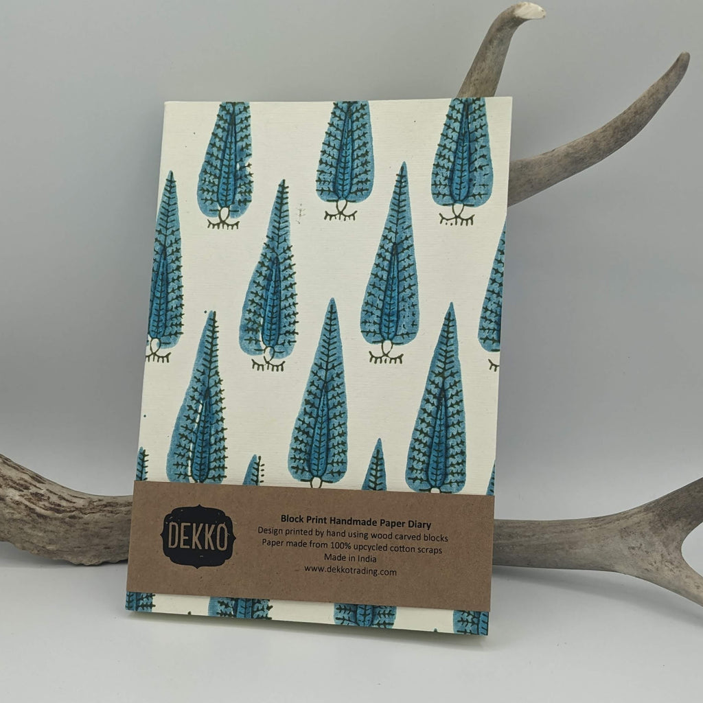 A handcrafted journal with a turquoise peacock stamp design, placed against a neutral backdrop with antlers in the frame.