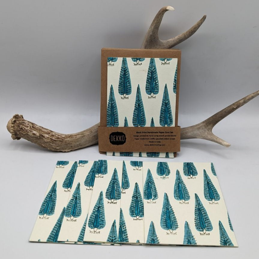 A set of handcrafted cards with a turquoise peacock stamp design, accompanied by kraft paper envelopes, displayed in a natural setting with antlers in the background.