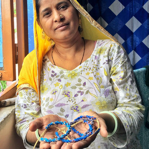 A woman wearing a yellow head scarf holding handmade bracelets