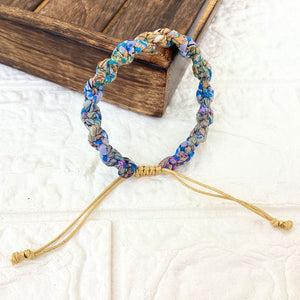 Woven bracelet in shades of light blue and gold on a wood tray.