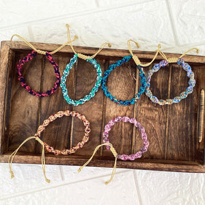 Six brightly colored bracelets on a wooden tray with a white background