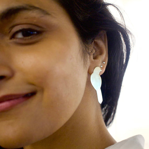 Close-up of a woman wearing a shiny gold toned bird earring with a blurred background