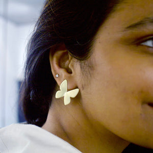 Close-up of a person wearing a gold toned butterfly-shaped earring.