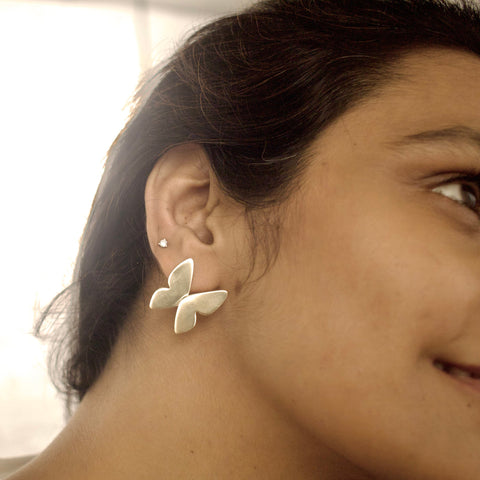 Close-up of a person wearing butterfly-shaped earrings with a blurred background
