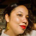 Load image into Gallery viewer, Close-up of a person with curly hair wearing a gold toned, gingko leaf shaped earring and red lipstick.
