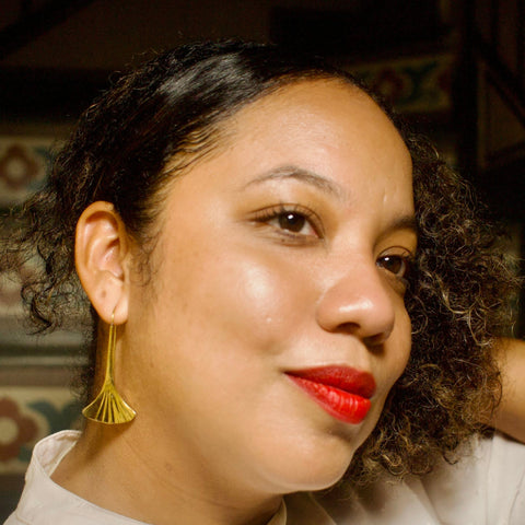 Close-up of a person with curly hair wearing a gold toned, gingko leaf shaped earring and red lipstick.