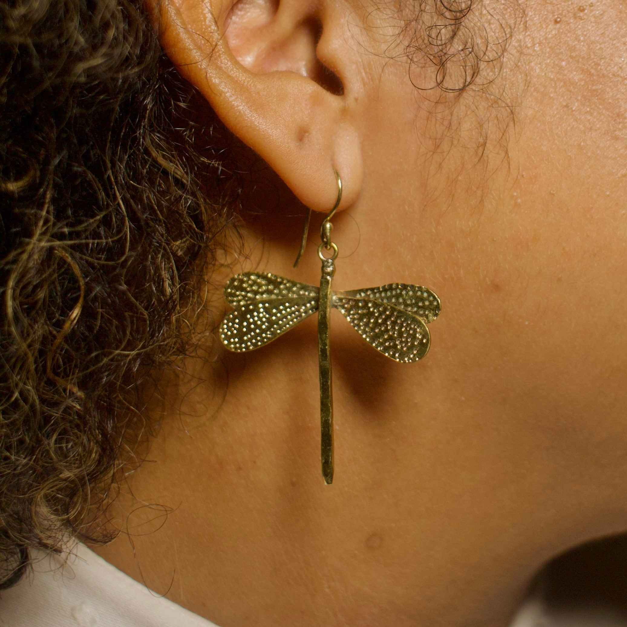 Close-up of a person wearing a gold dragonfly earring.