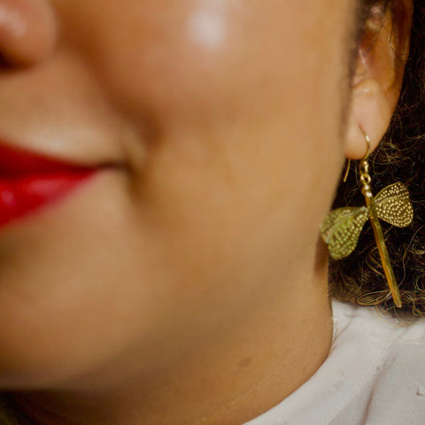Close-up of a person wearing gold  toned dragonfly shaped earrings