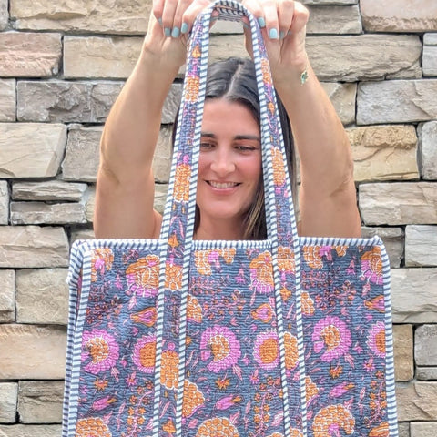 Person holding a floral-patterned tote bag against a stone wall.