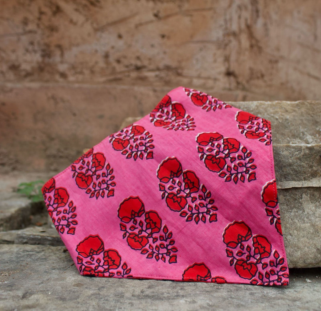 Pink bandana bib with red floral pattern on a stone surface
