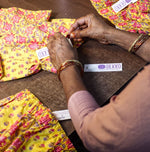 Load image into Gallery viewer, Person packaging yellow floral children's pants with 'DEKKO' labels on a wooden surface.
