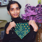 Load image into Gallery viewer, Person holding a green and yellow patterned bandana bib in a room with colorful yarn.
