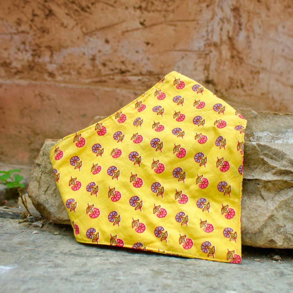 Yellow quilted bandana bib with floral pattern on a stone surface