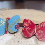 Load image into Gallery viewer, Two butterfly-shaped hair clips, one blue and one red, on a wooden surface.
