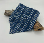 Load image into Gallery viewer, Blue bib with white patterns folded on a white surface with wooden elements.
