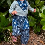 Load image into Gallery viewer, Child wearing a blue and white patterned outfit standing among green leaves.
