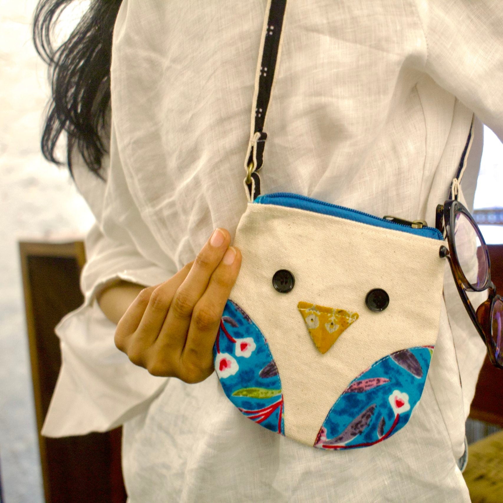 Person holding a small owl-shaped bag with a colorful design.