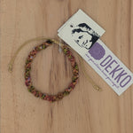 Load image into Gallery viewer, Handmade bracelet in shades of pink and gold on a wooden background with a label that says Dekko
